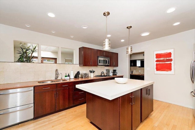 kitchen with light wood-type flooring, stainless steel appliances, sink, a center island, and hanging light fixtures