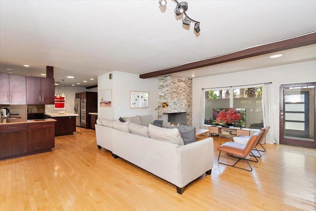 living room featuring beam ceiling, light hardwood / wood-style floors, a stone fireplace, and sink