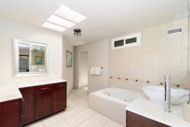 bathroom with a skylight, vanity, tiled tub, tile walls, and tile patterned flooring