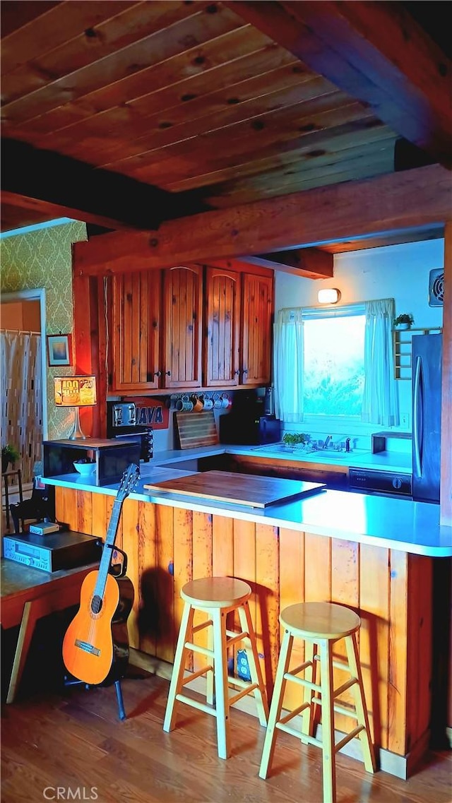 kitchen featuring a kitchen breakfast bar, kitchen peninsula, black fridge, and wood-type flooring