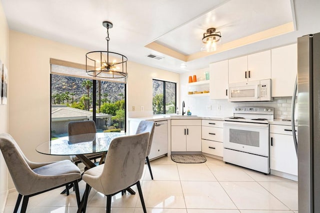 kitchen with white appliances, pendant lighting, white cabinetry, sink, and a raised ceiling