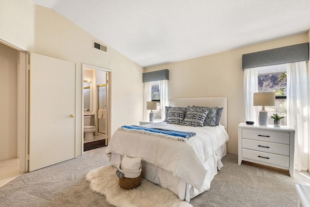 bedroom with light colored carpet, connected bathroom, and lofted ceiling