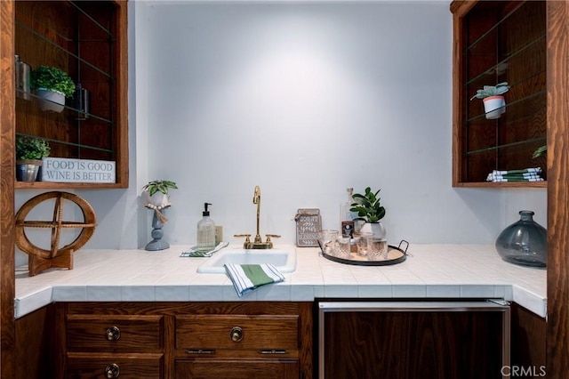 bar featuring dark brown cabinetry, tile counters, and sink