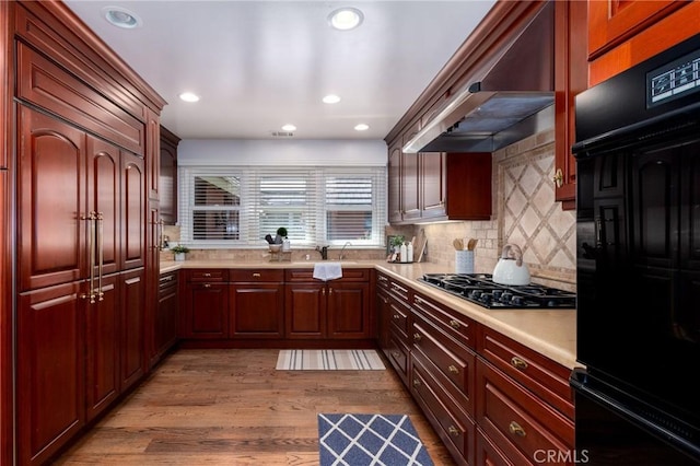 kitchen with backsplash, wall chimney exhaust hood, sink, light hardwood / wood-style flooring, and stainless steel gas stovetop