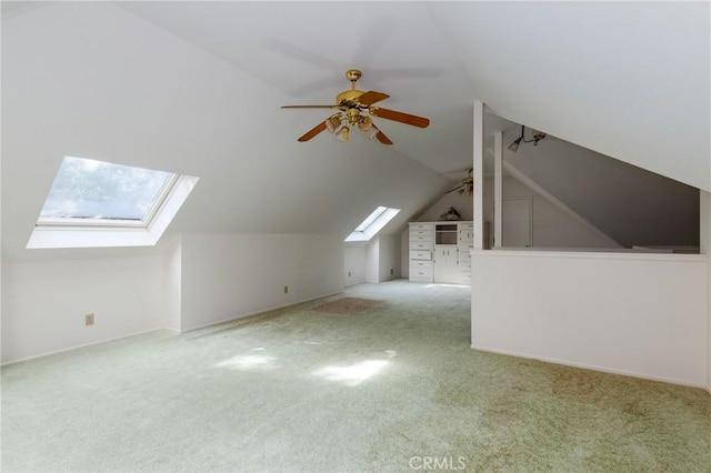 additional living space featuring vaulted ceiling with skylight, ceiling fan, and light colored carpet