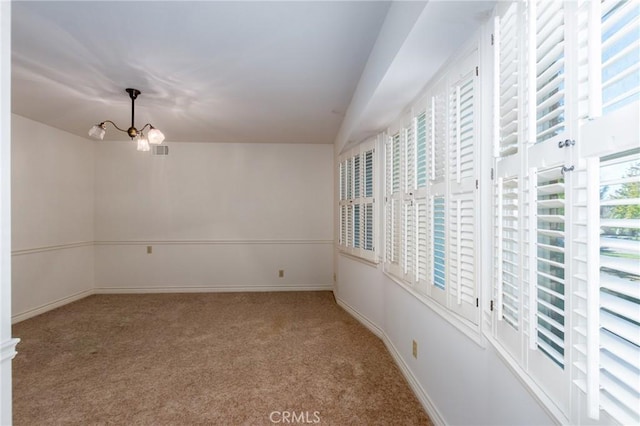 carpeted spare room with an inviting chandelier