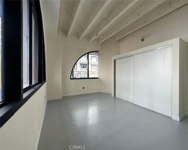 unfurnished room with beamed ceiling and concrete floors