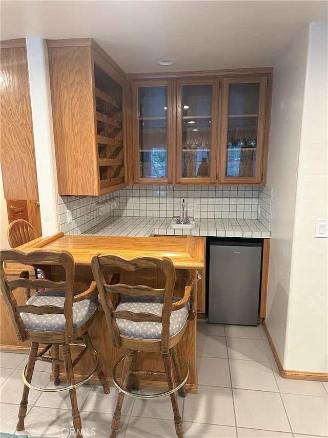 bar featuring decorative backsplash, sink, light tile patterned floors, and refrigerator