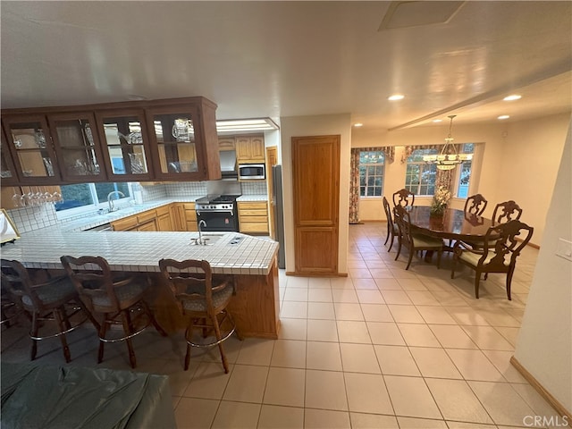 kitchen with black gas range, light tile patterned floors, kitchen peninsula, stainless steel microwave, and a breakfast bar