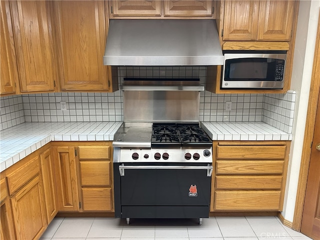 kitchen featuring decorative backsplash, stainless steel appliances, tile countertops, and range hood