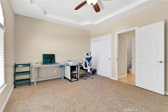 office area with ceiling fan, light colored carpet, and a tray ceiling