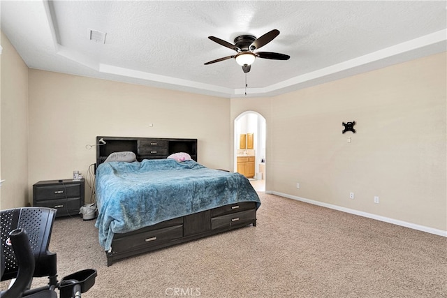 bedroom featuring light colored carpet, a raised ceiling, ceiling fan, and ensuite bathroom