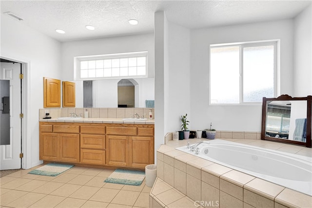 bathroom featuring vanity, tile patterned floors, a textured ceiling, and a relaxing tiled tub