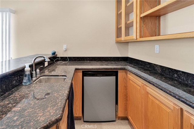 kitchen featuring dark stone counters, sink, light tile patterned floors, and stainless steel dishwasher