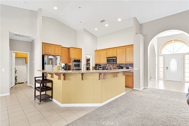 kitchen with light tile patterned flooring, a center island with sink, backsplash, stainless steel appliances, and a breakfast bar