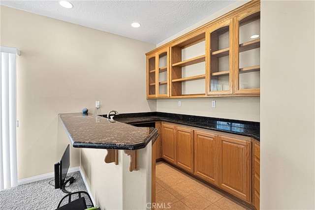 kitchen with a kitchen breakfast bar, dark stone countertops, kitchen peninsula, a textured ceiling, and sink