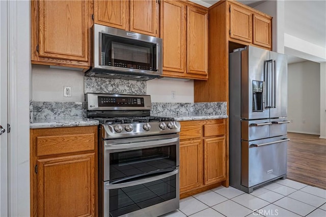 kitchen with light tile patterned flooring, light stone countertops, and appliances with stainless steel finishes