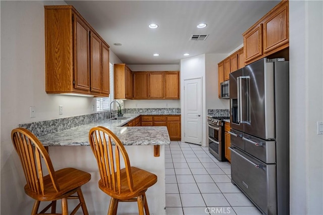 kitchen featuring sink, kitchen peninsula, a breakfast bar area, light tile patterned floors, and appliances with stainless steel finishes