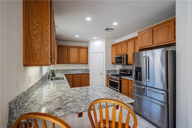 kitchen featuring kitchen peninsula, appliances with stainless steel finishes, a kitchen bar, sink, and light tile patterned floors