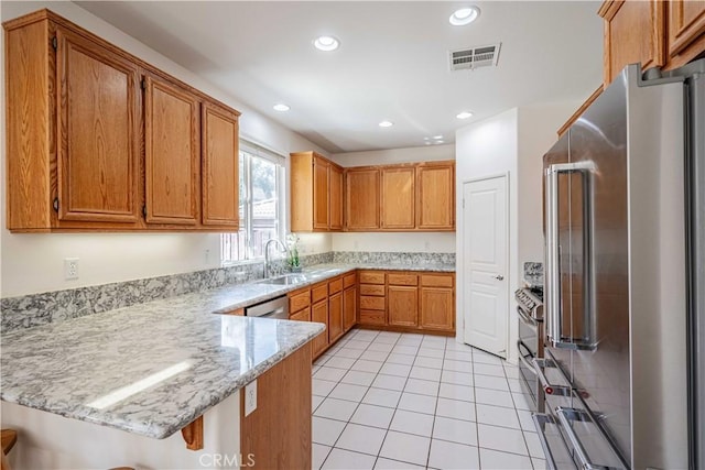 kitchen with kitchen peninsula, a kitchen bar, light stone countertops, stainless steel appliances, and sink