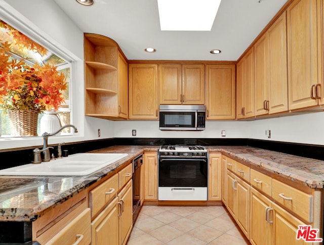 kitchen with stone countertops, sink, white gas range oven, and a skylight