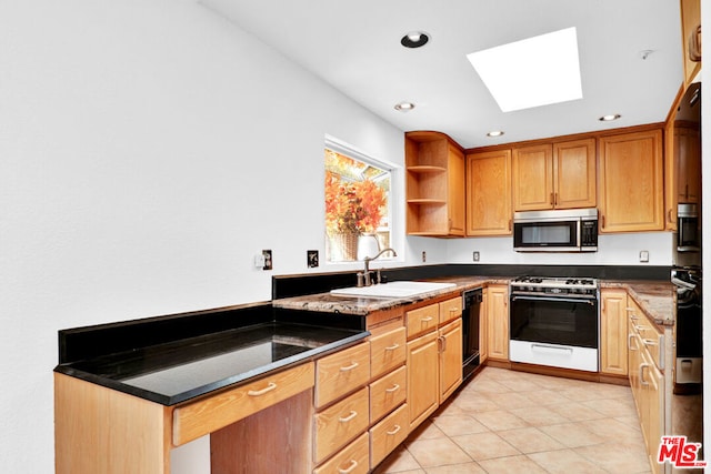 kitchen with dark stone counters, black appliances, sink, a skylight, and light tile patterned floors