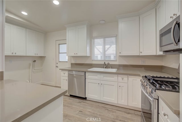 kitchen with stainless steel appliances, white cabinetry, light wood-type flooring, and sink