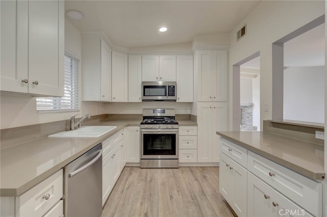 kitchen with light hardwood / wood-style floors, vaulted ceiling, white cabinets, stainless steel appliances, and sink