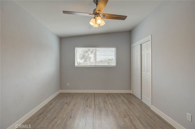 unfurnished bedroom featuring ceiling fan, a closet, light wood-type flooring, and vaulted ceiling