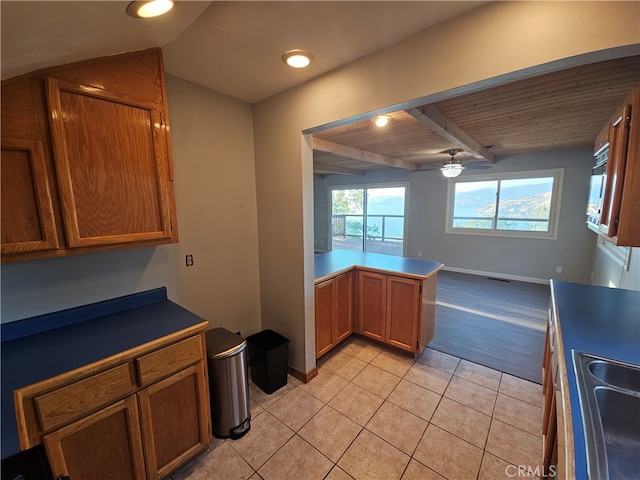 kitchen featuring beamed ceiling, kitchen peninsula, light tile patterned floors, ceiling fan, and wooden ceiling