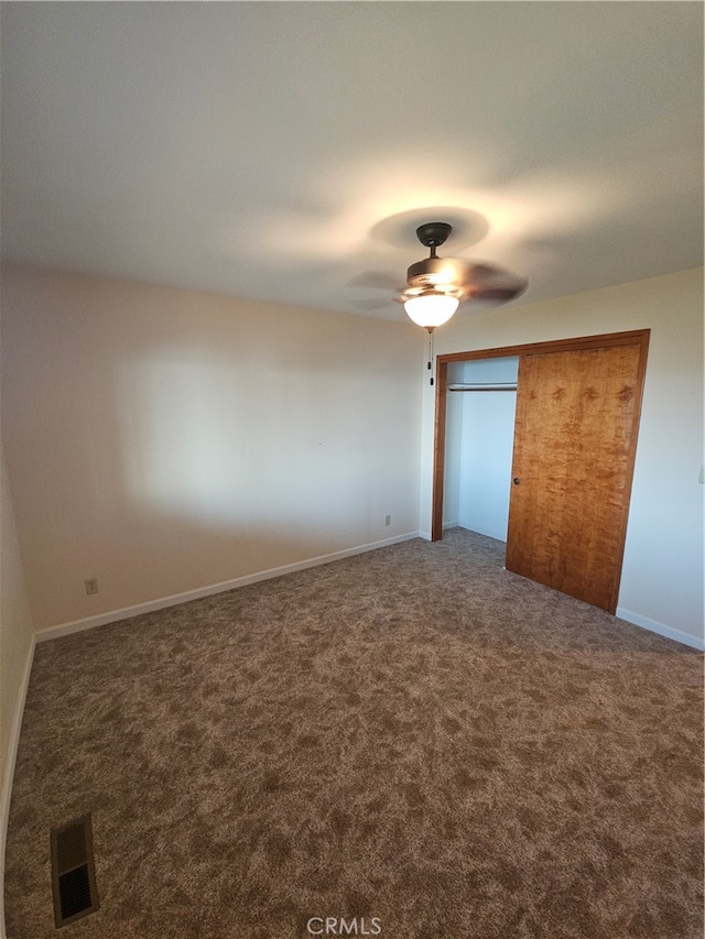 unfurnished bedroom with dark colored carpet, ceiling fan, and a closet