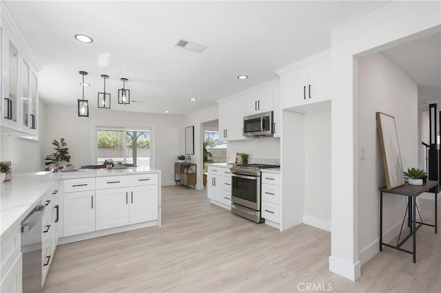 kitchen with white cabinets, appliances with stainless steel finishes, decorative light fixtures, and light hardwood / wood-style flooring