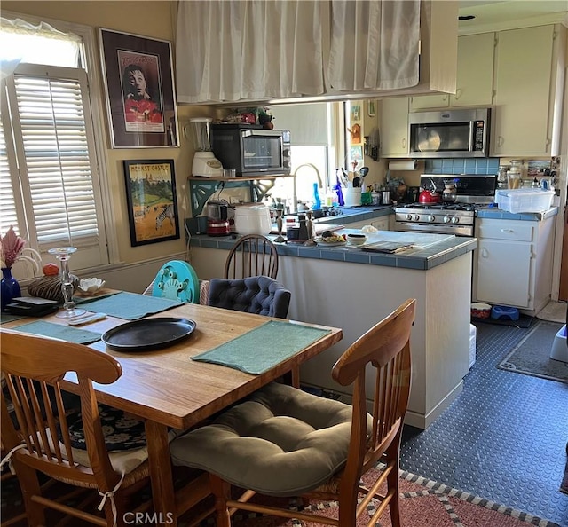 kitchen featuring white cabinets, stainless steel appliances, tile counters, and a healthy amount of sunlight