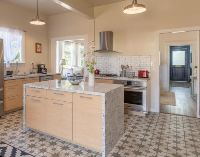 kitchen featuring wall chimney range hood, a kitchen island, pendant lighting, sink, and appliances with stainless steel finishes