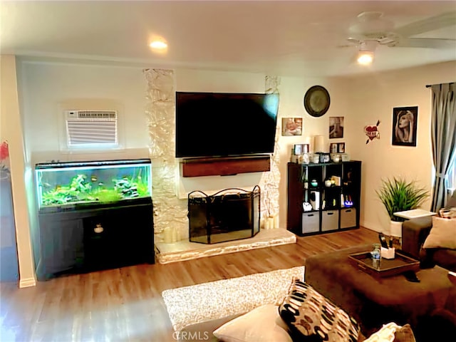 living room featuring light hardwood / wood-style floors, a wall mounted air conditioner, ceiling fan, and a stone fireplace