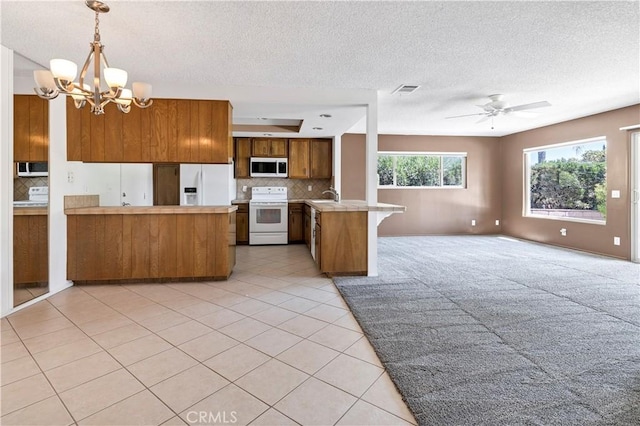 kitchen featuring white appliances, ceiling fan with notable chandelier, hanging light fixtures, tasteful backsplash, and kitchen peninsula