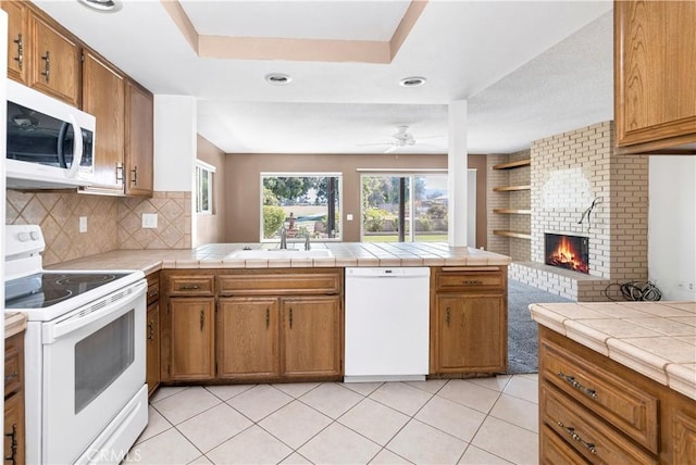 kitchen featuring a fireplace, white appliances, tile countertops, and sink