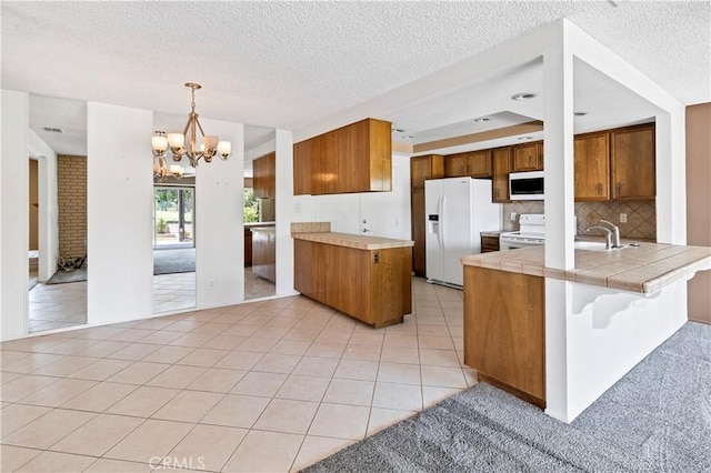 kitchen featuring kitchen peninsula, light tile patterned flooring, white appliances, and an inviting chandelier