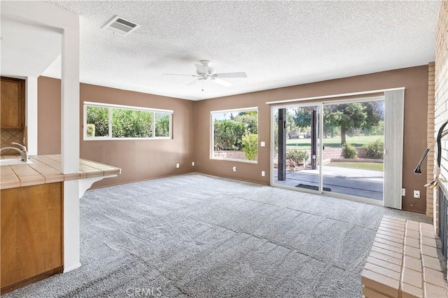 unfurnished living room featuring sink, light colored carpet, and a textured ceiling