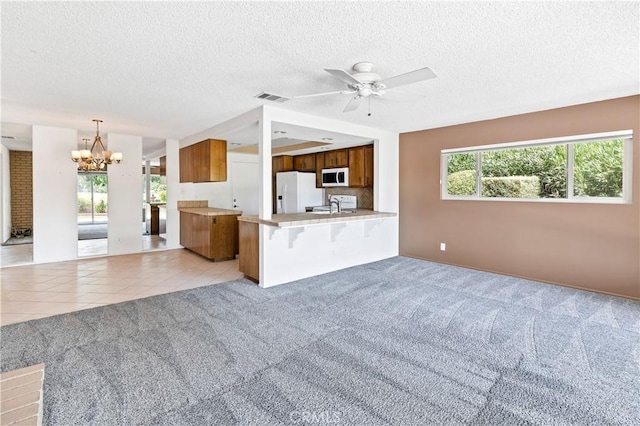 unfurnished living room with light carpet, a textured ceiling, and ceiling fan with notable chandelier