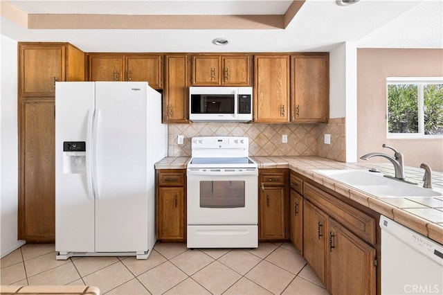 kitchen featuring tasteful backsplash, white appliances, sink, light tile patterned floors, and tile countertops