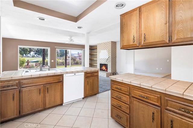 kitchen featuring a fireplace, ceiling fan, sink, dishwasher, and tile counters