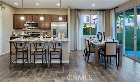 kitchen featuring hanging light fixtures, a center island with sink, dark wood-type flooring, stainless steel appliances, and a breakfast bar area