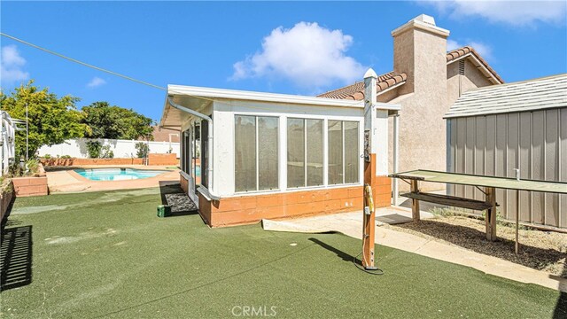 rear view of house with a lawn, a storage unit, a sunroom, and a fenced in pool