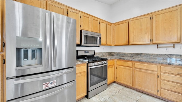 kitchen featuring dark stone countertops, light brown cabinetry, appliances with stainless steel finishes, and light tile patterned floors