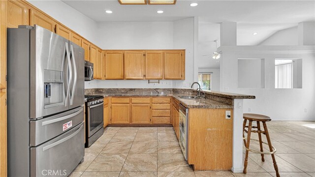 kitchen featuring appliances with stainless steel finishes, a breakfast bar, kitchen peninsula, dark stone counters, and sink