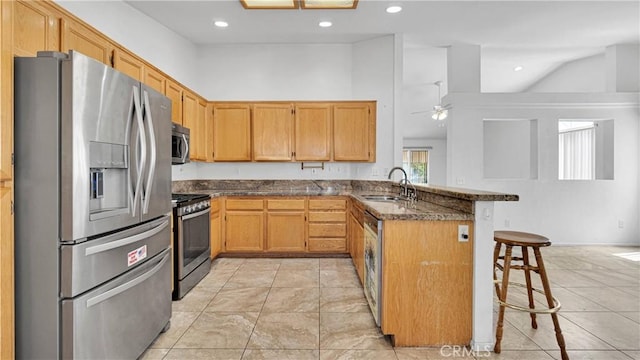 kitchen with stainless steel appliances, a peninsula, a sink, dark stone countertops, and a breakfast bar area