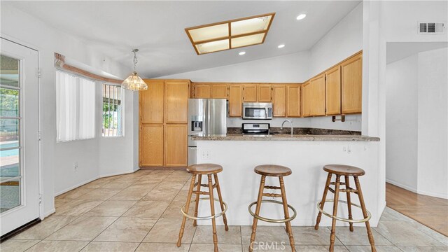 kitchen with vaulted ceiling, a breakfast bar area, pendant lighting, and stainless steel appliances