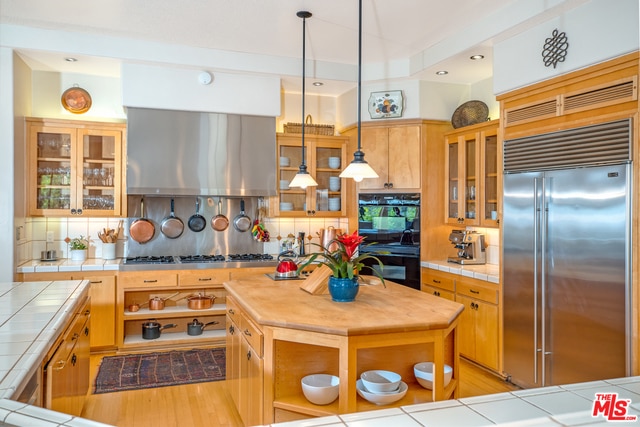 kitchen featuring decorative light fixtures, ventilation hood, tile counters, stainless steel appliances, and decorative backsplash