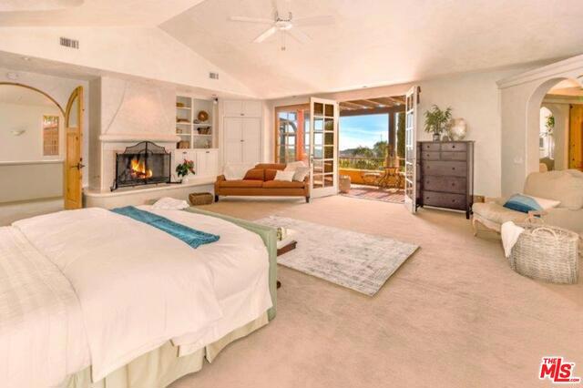 carpeted bedroom featuring vaulted ceiling, a large fireplace, access to exterior, and ceiling fan